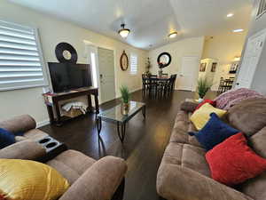 Living area featuring arched walkways, dark wood finished floors, vaulted ceiling, a textured ceiling, and baseboards