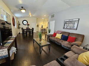 Living area featuring lofted ceiling, dark wood-type flooring, a textured ceiling, and visible vents