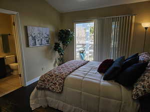 Bedroom with access to exterior, dark wood finished floors, lofted ceiling, ensuite bath, and baseboards