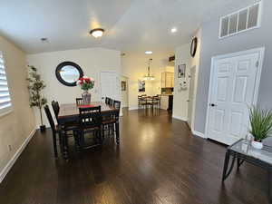 Dining space with dark wood-style floors, baseboards, visible vents, and vaulted ceiling