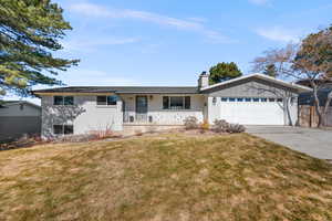 Ranch-style home with driveway, an attached garage, a chimney, and a front lawn