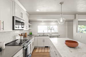 Kitchen with light stone counters, hanging light fixtures, appliances with stainless steel finishes, white cabinets, and a sink