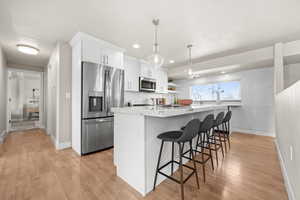 Kitchen with pendant lighting, a breakfast bar area, open shelves, appliances with stainless steel finishes, and white cabinets