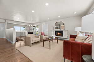 Living area featuring baseboards, a glass covered fireplace, wood finished floors, a chandelier, and recessed lighting