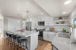 Kitchen with open shelves, appliances with stainless steel finishes, white cabinets, a kitchen island, and a sink