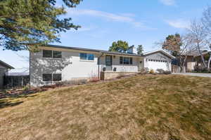 Ranch-style home with driveway, a chimney, a porch, an attached garage, and a front lawn