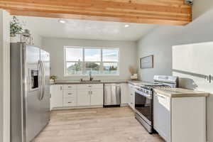 Kitchen featuring stainless steel appliances, light countertops, light wood-type flooring, white cabinetry, and a sink