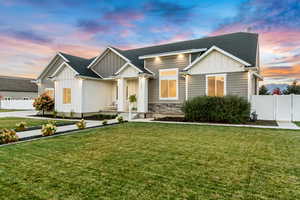 View of front facade featuring a shingled roof, fence, a front lawn, and board and batten siding