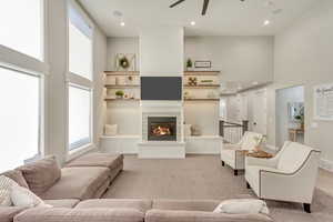 Living area with light carpet, a glass covered fireplace, a towering ceiling, and recessed lighting