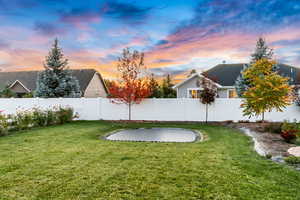 Yard at dusk with a trampoline and a fenced backyard