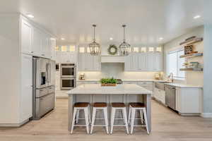 Kitchen featuring stainless steel appliances, glass insert cabinets, white cabinetry, and a center island