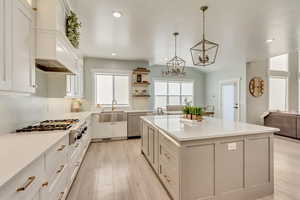 Kitchen featuring appliances with stainless steel finishes, a center island, hanging light fixtures, white cabinetry, and a sink