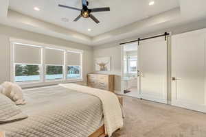 Bedroom with light carpet, a tray ceiling, and a barn door