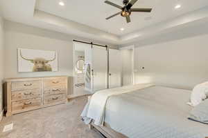 Bedroom featuring a tray ceiling, recessed lighting, light colored carpet, a barn door, and connected bathroom