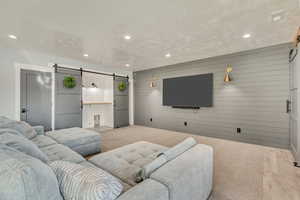 Carpeted living area with wooden walls, a barn door, and recessed lighting