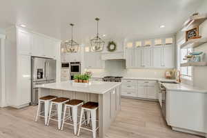 Kitchen with stainless steel appliances, a sink, white cabinetry, a center island, and open shelves