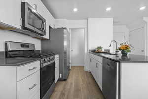 Kitchen featuring stainless steel appliances, dark countertops, white cabinets, and a sink