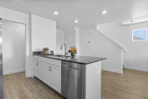 Kitchen featuring light wood finished floors, white cabinets, dark countertops, stainless steel dishwasher, and a sink