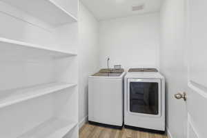 Clothes washing area featuring laundry area, visible vents, baseboards, light wood-style flooring, and washer and dryer