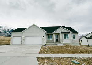 View of front of property with a mountain view, a garage, driveway, stone siding, and board and batten siding