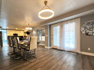 Dining room featuring dark wood-style floors, visible vents, a textured ceiling, and baseboards