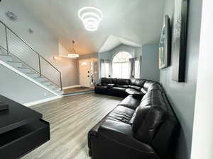 Living room with lofted ceiling, light wood-type flooring, stairs, and a textured ceiling