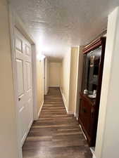 Hallway with dark wood-style flooring, a textured ceiling, and baseboards