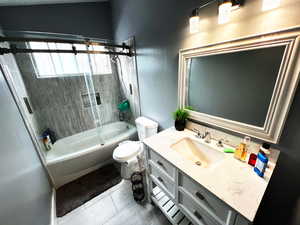 Bathroom with toilet, tile patterned flooring, enclosed tub / shower combo, and vanity