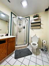 Full bath with toilet, a shower stall, vanity, tile patterned flooring, and baseboards