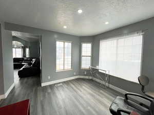 Office space with a textured ceiling, recessed lighting, wood finished floors, visible vents, and baseboards