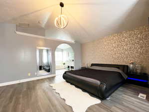 Bedroom featuring visible vents, arched walkways, wood finished floors, vaulted ceiling, and a textured ceiling