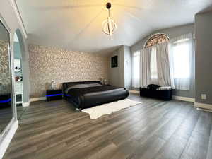 Bedroom featuring baseboards, dark wood-type flooring, lofted ceiling, and wallpapered walls