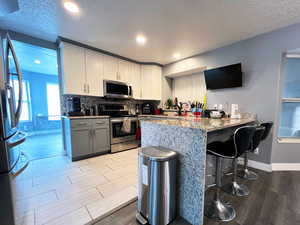Kitchen with a peninsula, light wood finished floors, white cabinets, and stainless steel appliances