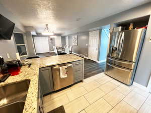 Kitchen with light stone countertops, gray cabinetry, appliances with stainless steel finishes, wood tiled floor, and pendant lighting