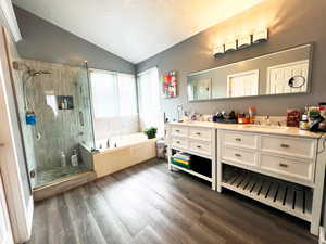Bathroom featuring lofted ceiling, wood finished floors, a sink, a bath, and double vanity