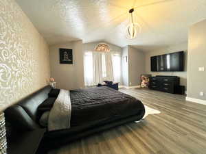 Bedroom with a textured ceiling, baseboards, vaulted ceiling, and wood finished floors