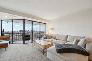 Living room featuring a textured ceiling, carpet floors, floor to ceiling windows, and a city view