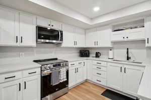 Kitchen featuring open shelves, stainless steel appliances, light countertops, white cabinets, and a sink