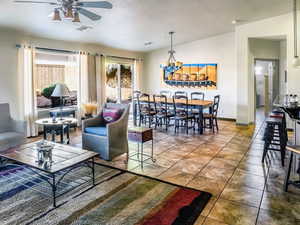 Living area featuring lofted ceiling, ceiling fan with notable chandelier, visible vents, baseboards, and tile patterned floors