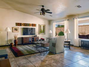 Living room with lofted ceiling, tile patterned flooring, visible vents, and ceiling fan