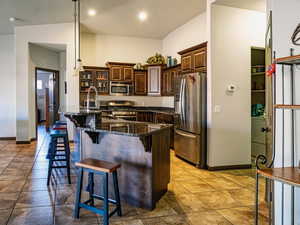 Kitchen featuring light tile patterned floors, a breakfast bar area, appliances with stainless steel finishes, dark stone counters, and a center island with sink