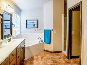 Bathroom featuring a garden tub, vanity, baseboards, and tile patterned floors