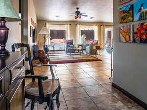 Tiled living area with ceiling fan, a textured ceiling, visible vents, and baseboards