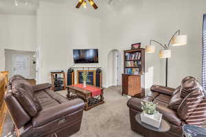 Carpeted living room featuring high vaulted ceiling, arched walkways, a glass covered fireplace, and baseboards