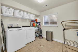 Laundry room with washing machine and clothes dryer, light tile patterned floors, visible vents, laundry area, and baseboards