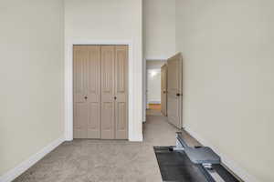 Workout room with baseboards, a high ceiling, visible vents, and light colored carpet