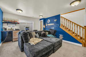 Living room featuring baseboards, stairway, indoor wet bar, and light colored carpet