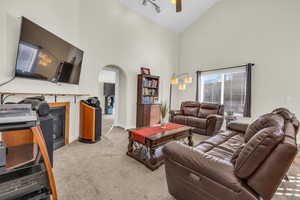 Living area featuring light carpet, arched walkways, baseboards, a glass covered fireplace, and ceiling fan