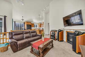 Living area with light carpet, high vaulted ceiling, track lighting, and a glass covered fireplace