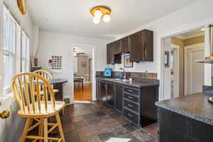 Kitchen featuring dark brown cabinetry, stone tile floors, dark countertops, ceiling fan, and a sink